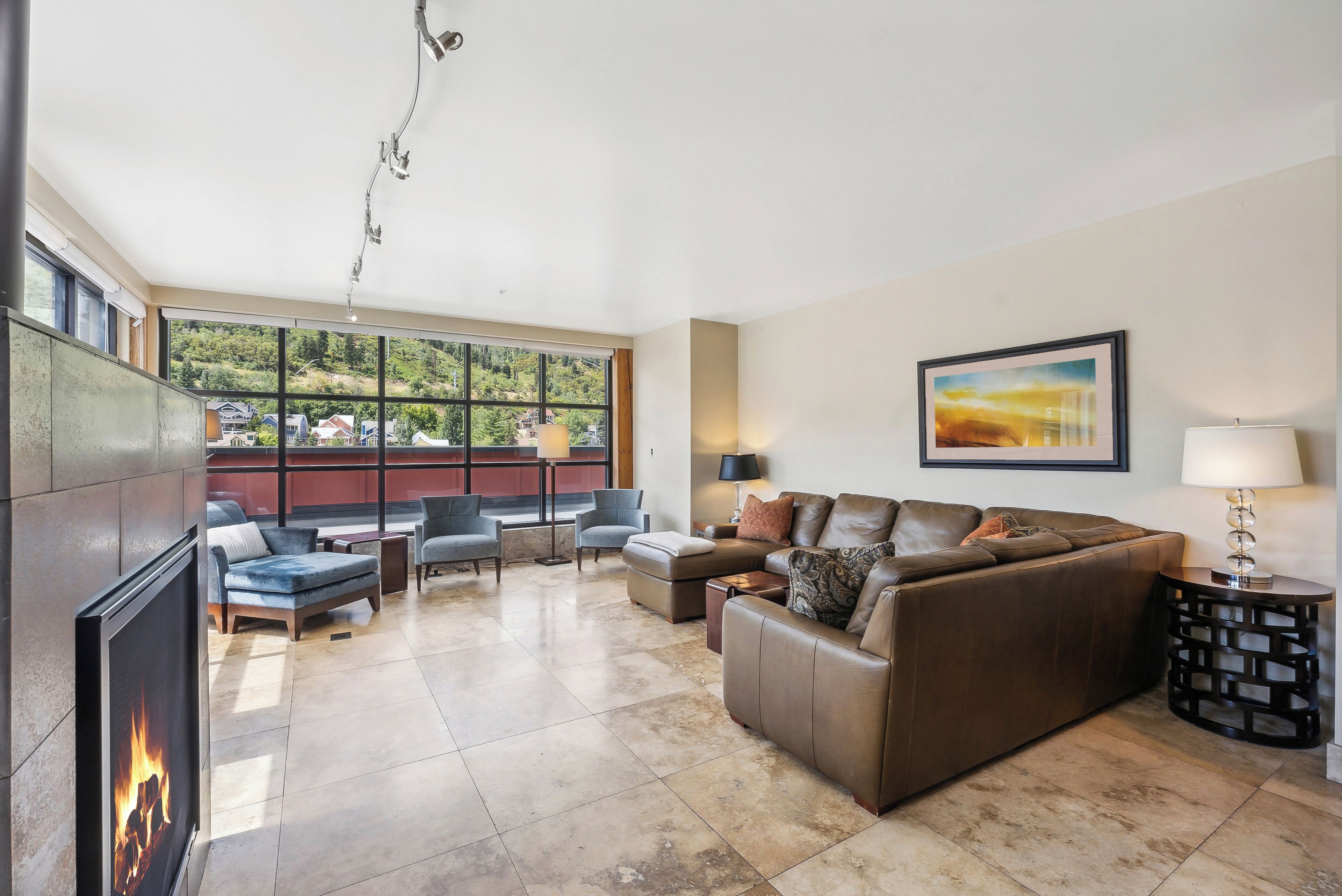 A spacious living room with a fireplace, comfortable seating, a large window with a view, and a framed artwork on the wall.