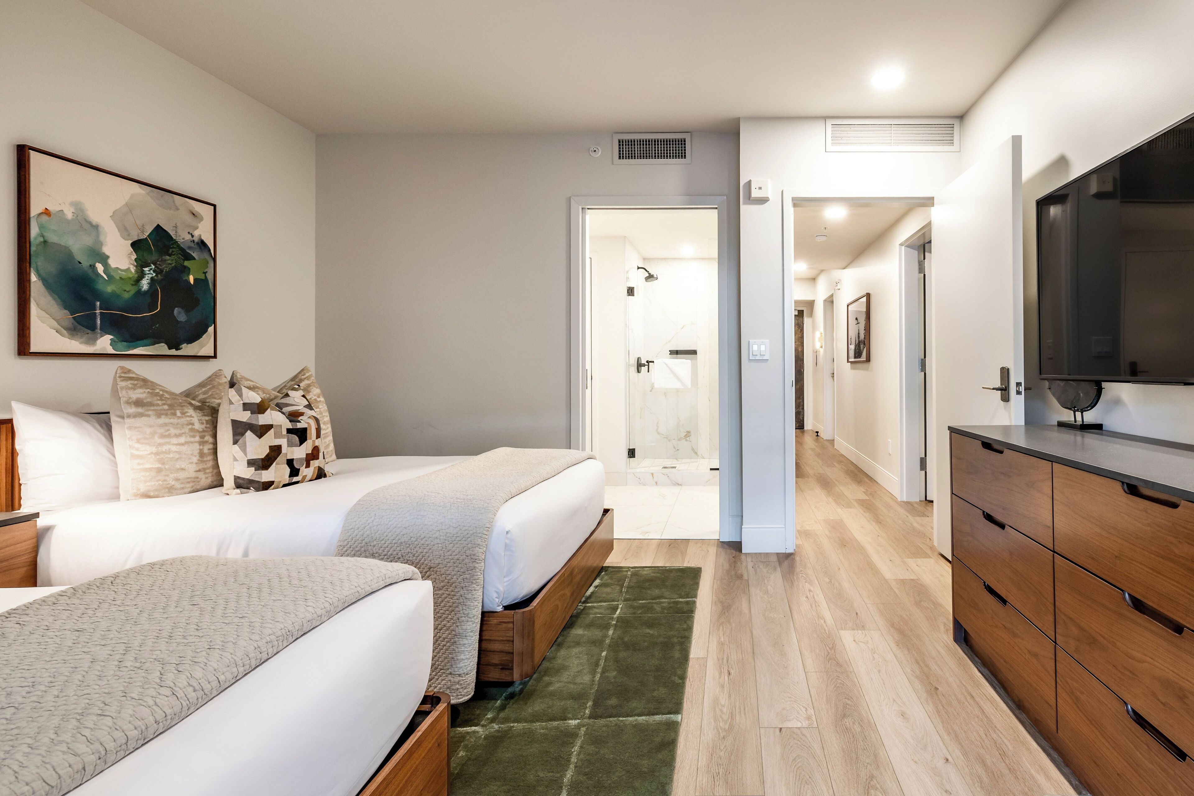 Ein modernes Schlafzimmer mit zwei Betten, einem grünen Teppich, Holzschränken und einem Bild an der Wand.