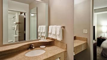 Une salle de bain d’hôtel avec un lavabo doté d’un plan de travail en granit, un grand miroir et un porte-serviettes muni de plusieurs serviettes.