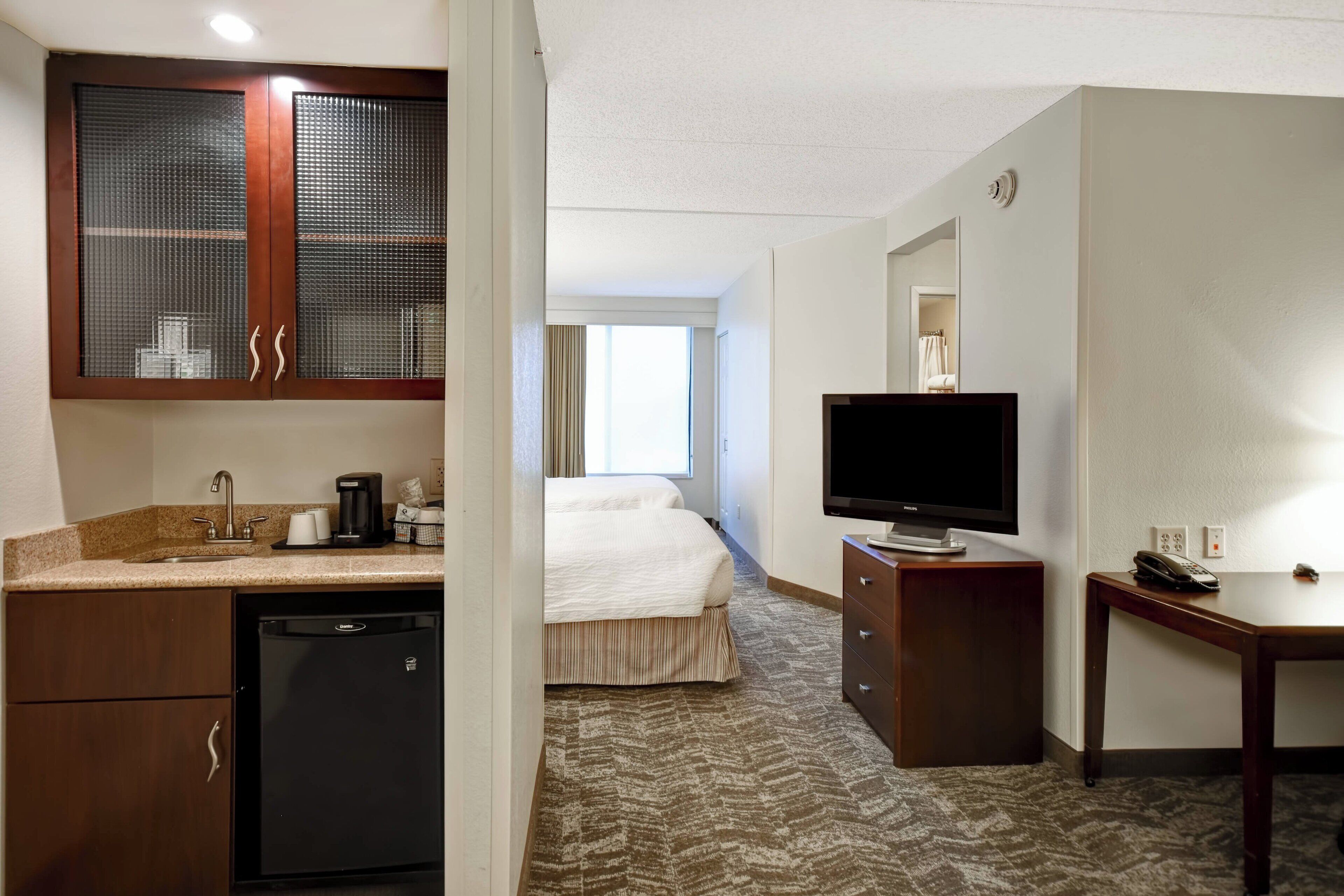 A hotel room with a kitchenette, a bed, a television, and a desk.