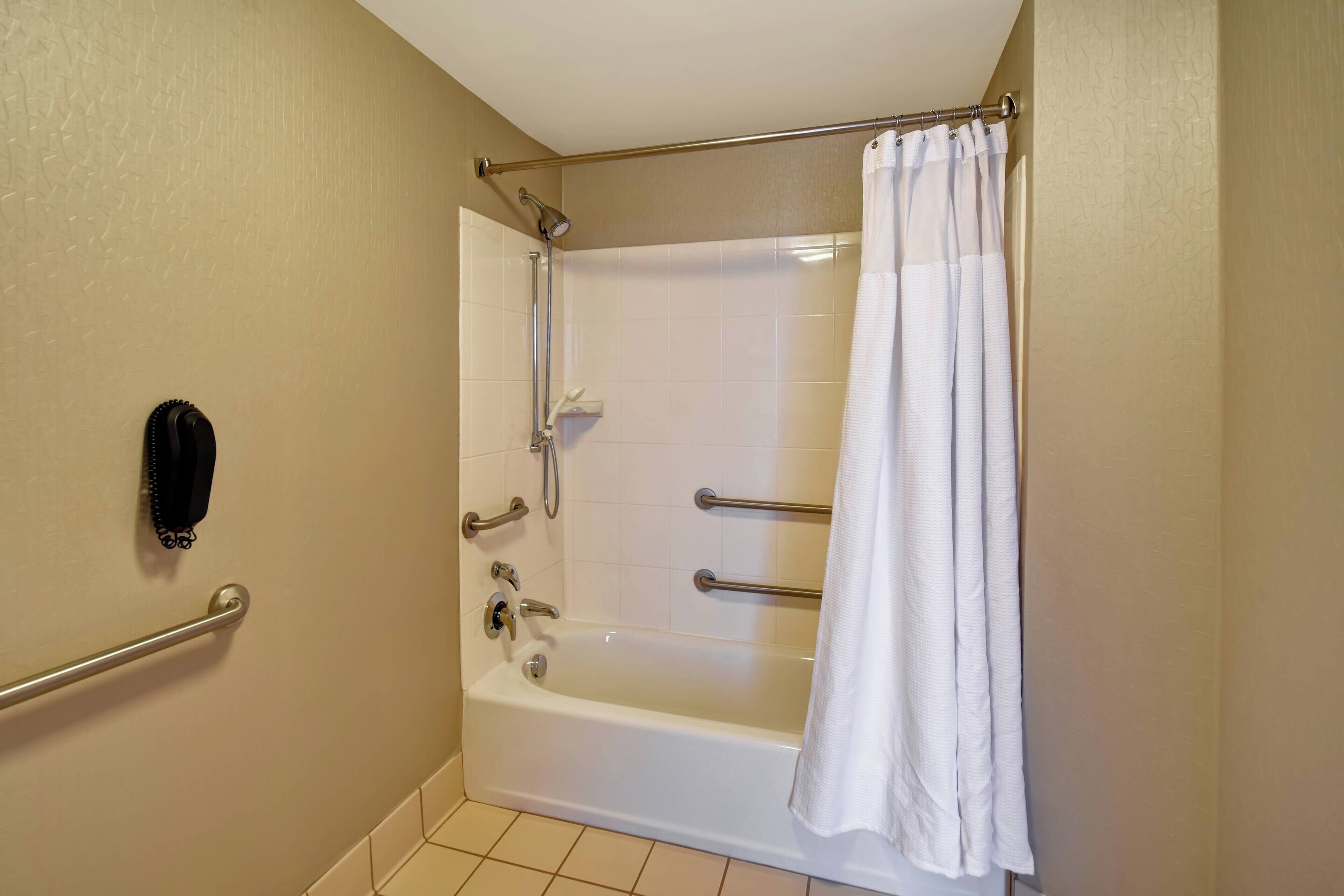Une salle de bain avec une baignoire blanche, un rideau de douche, un porte-serviettes et un sèche-mains.