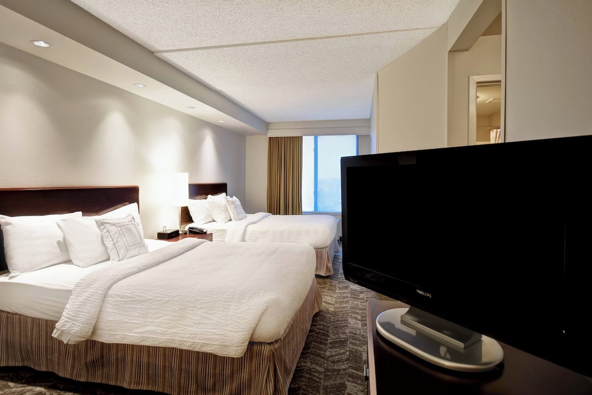 A hotel room with two beds, a television, and a bathroom visible through an open door.