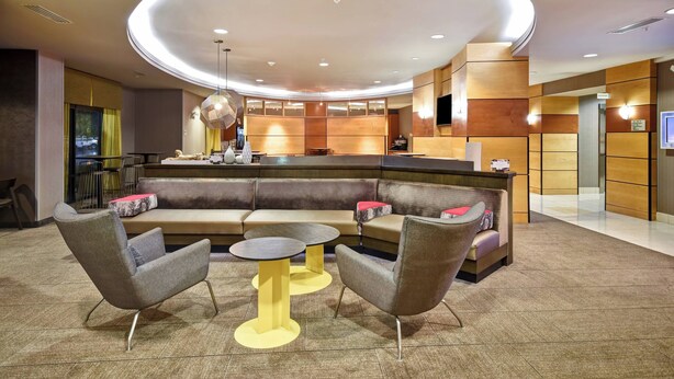 A modern lobby with a curved reception desk, seating area with sofas and armchairs, and a central coffee table. - Springhill Suites by Marriott Louisville Airport (Louisville)