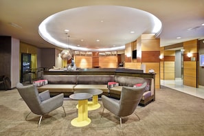 A modern lobby with a curved reception desk, seating area with sofas and armchairs, and a central coffee table. - Springhill Suites by Marriott Louisville Airport (Louisville)