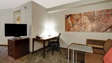 A hotel room with a flat-screen TV, a desk with a lamp, a brown leather sofa, and a marble coffee table.
