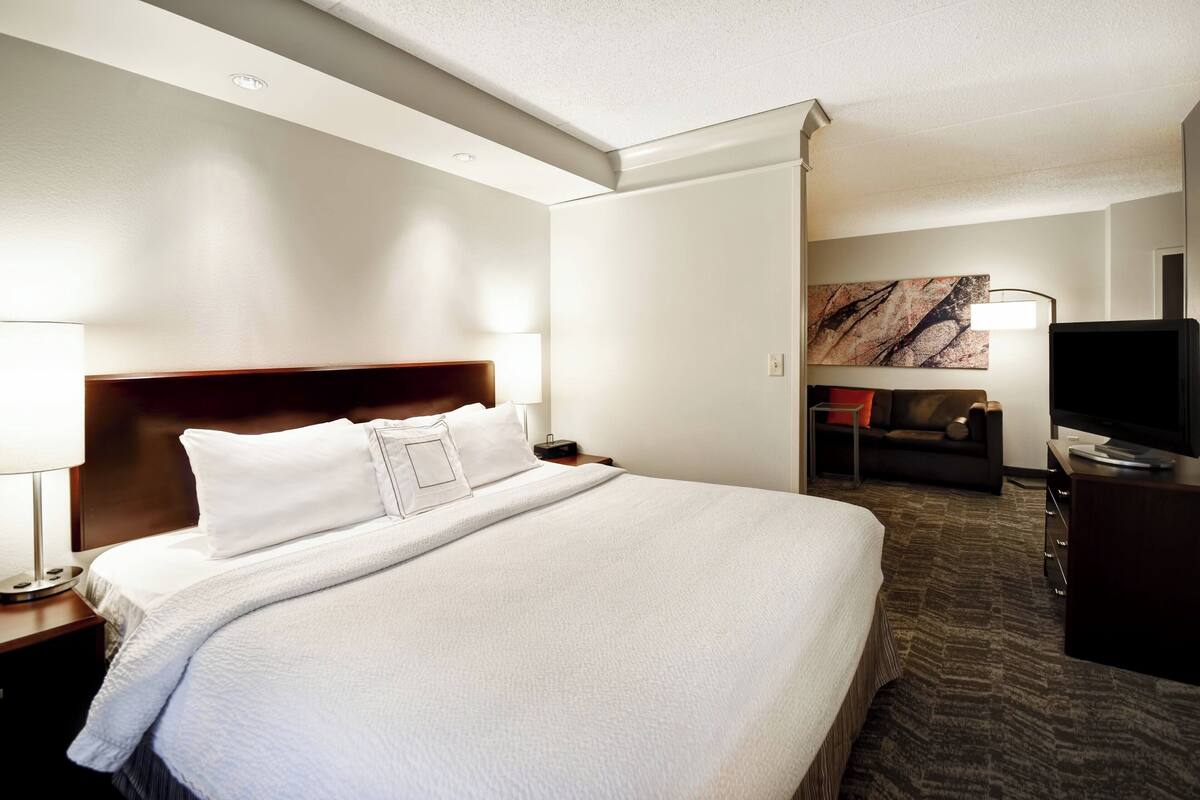 A hotel room with a large bed, a television, a desk, and a sofa.