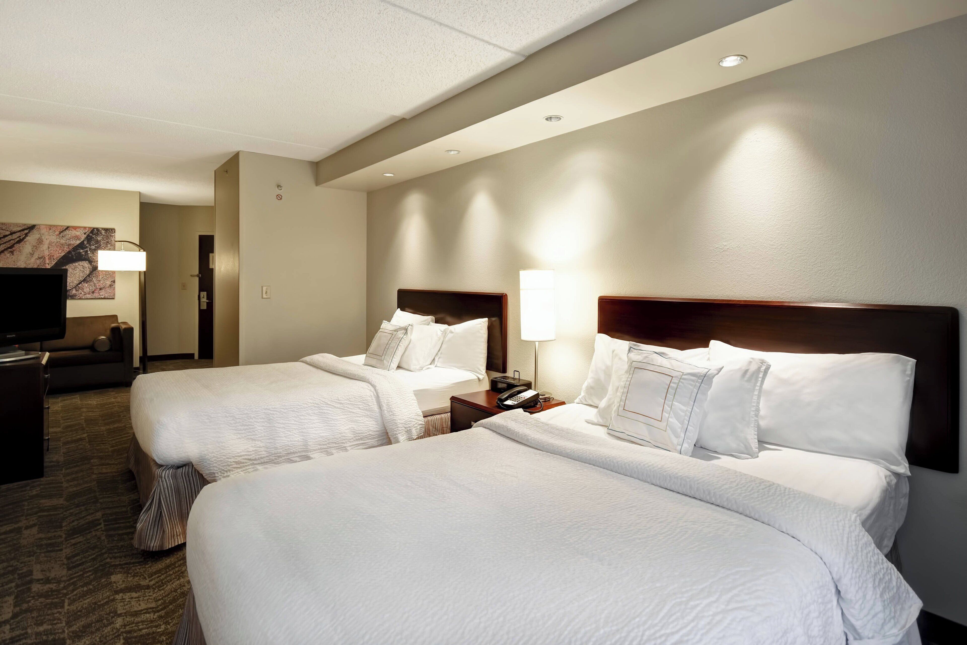 A hotel room with two beds, a TV, and a lamp.