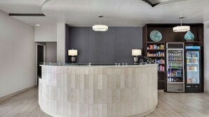 A reception area with a curved counter, two pendant lights, a refrigerator stocked with beverages, and a snack shelf. - SpringHill Suites by Marriott Jacksonville North I-95 Area (Jacksonville)