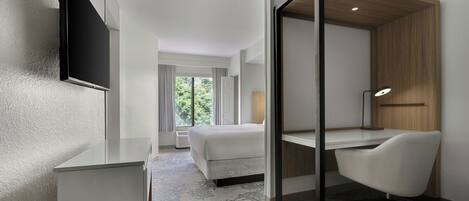 A modern hotel room with a bed, a desk, and a TV mounted on the wall.