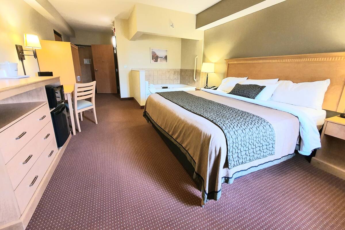 A hotel room with a bed, bedside tables, a desk with a chair, a small kitchenette, and a bathroom.