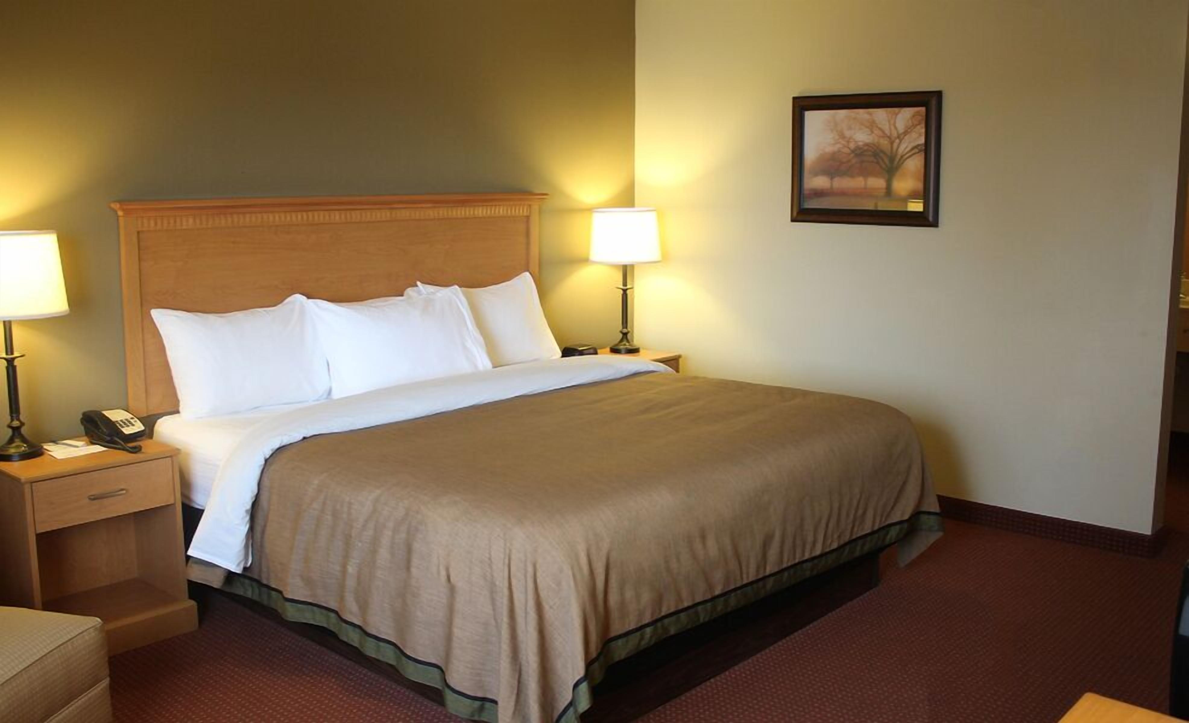 A hotel room with a large bed, two bedside tables with lamps, a nightstand, a chair, and a framed picture on the wall.