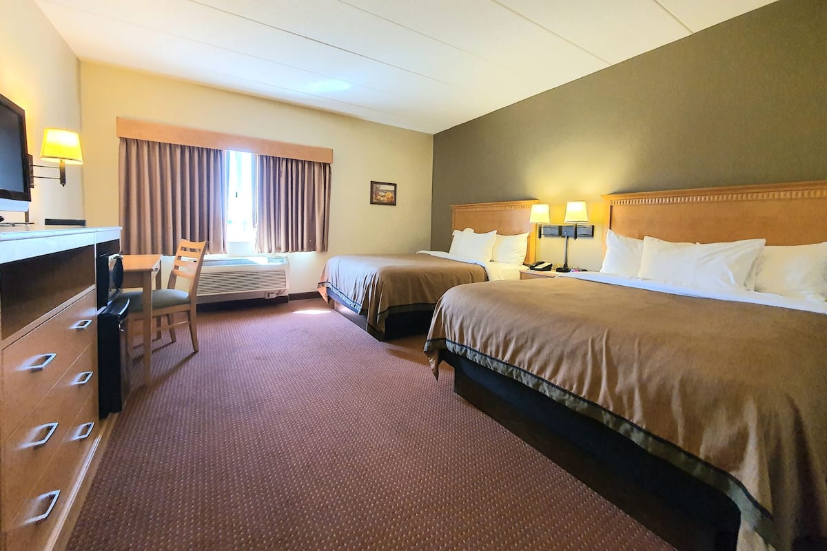 A hotel room with two beds, a desk, a chair, and a television.