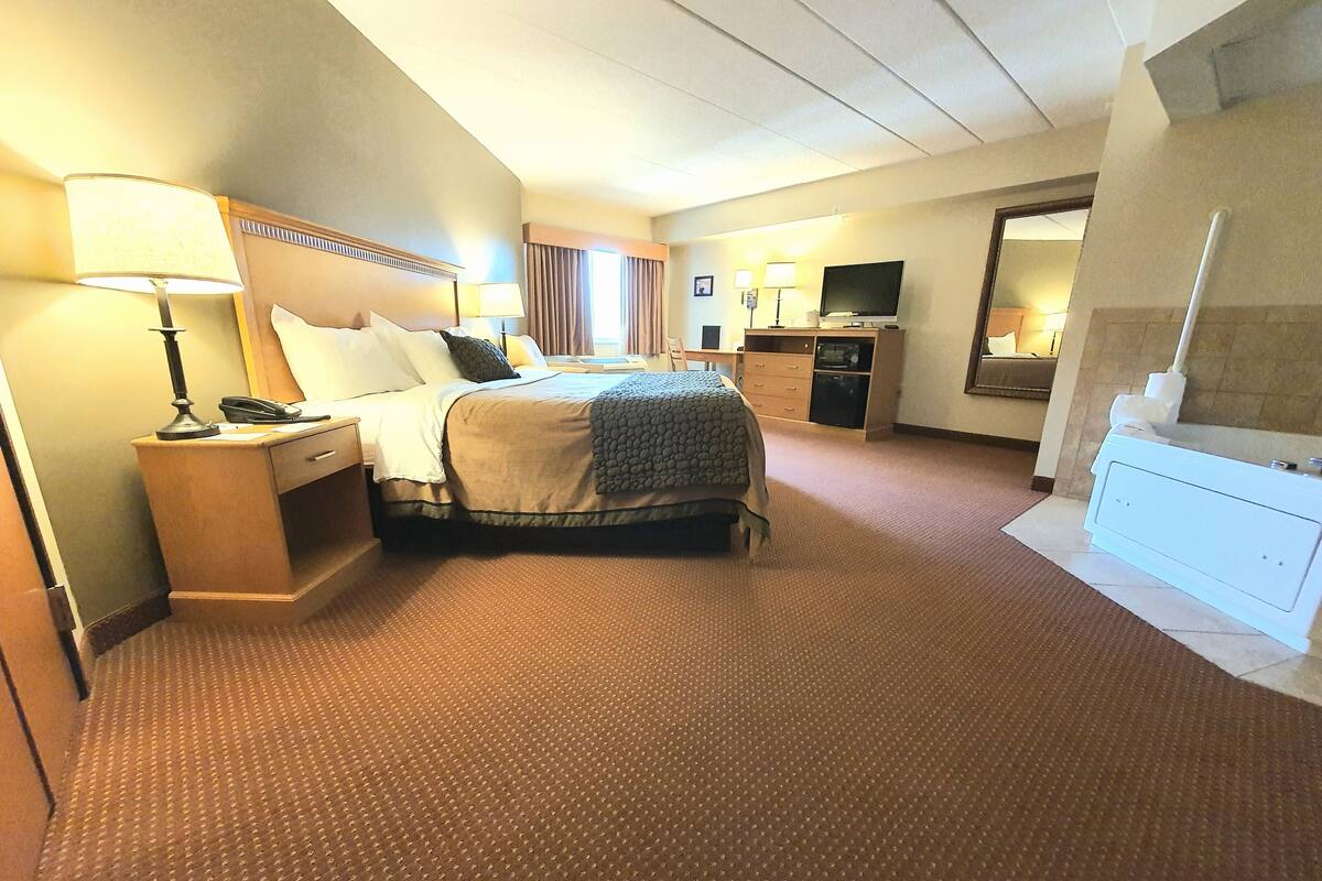 A hotel room with a large bed, bedside tables, a desk, a television, and a bathroom with a bathtub.