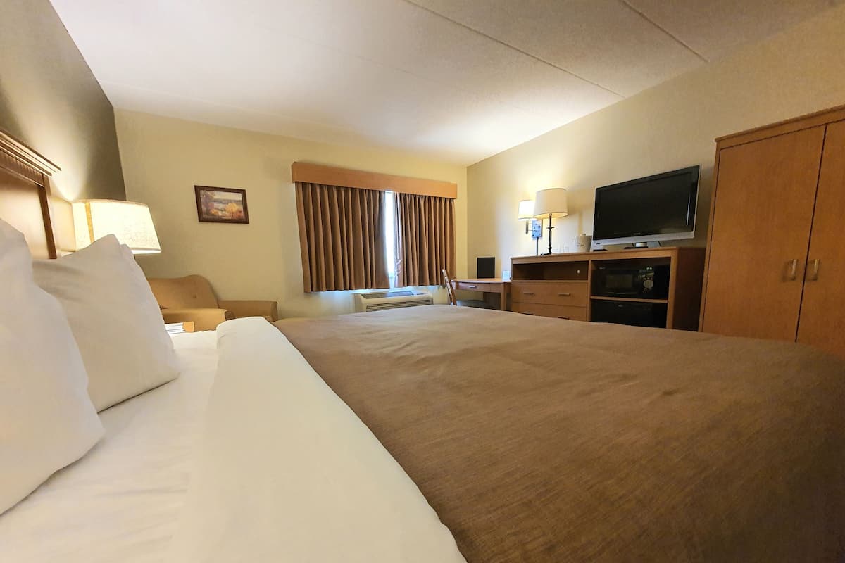 A hotel room with a large bed, a desk with a computer, a television, and a wardrobe.