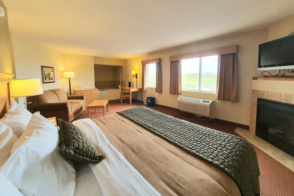 A hotel room with a bed, a desk, a chair, a television, a fireplace, and a window with curtains.
