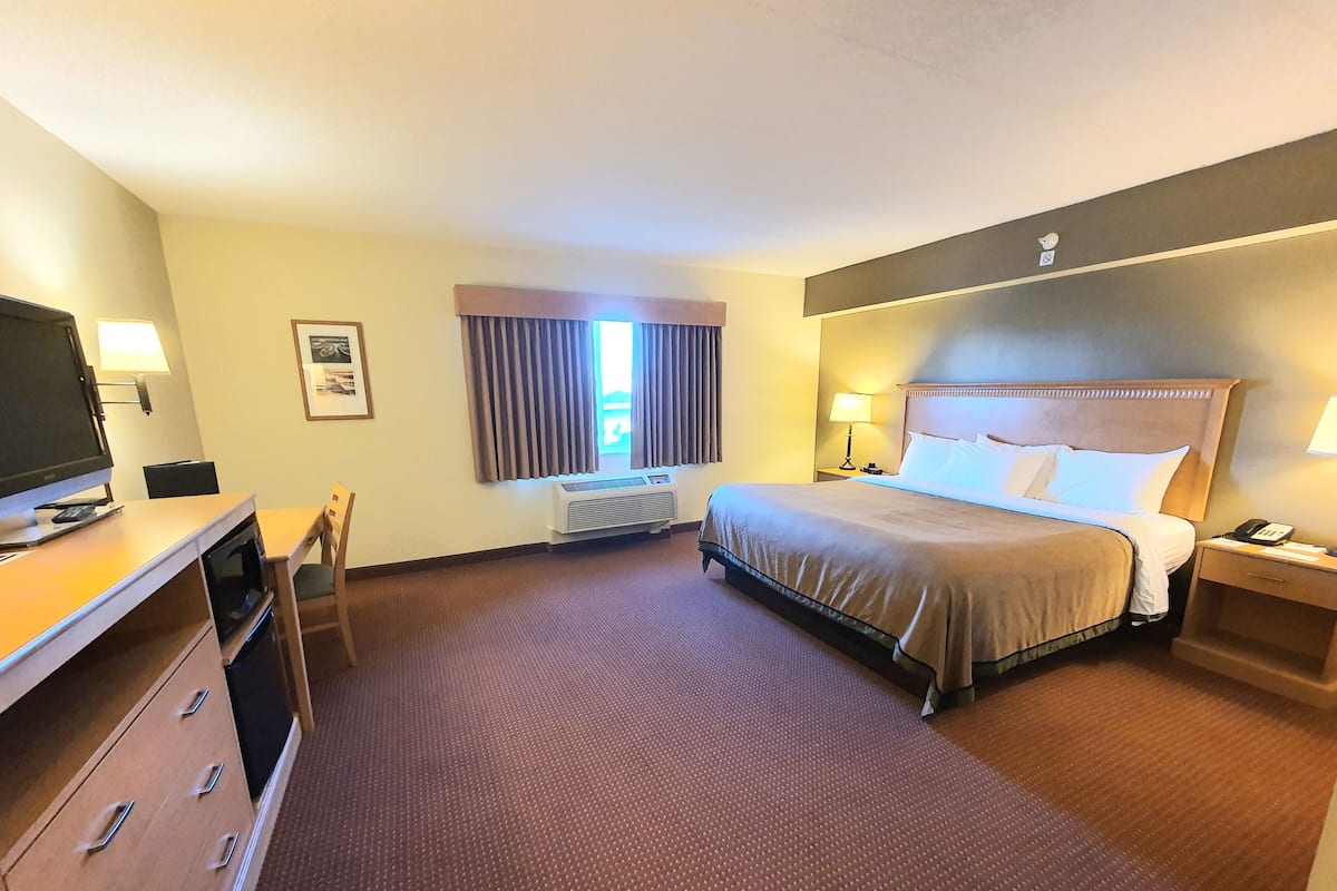 A hotel room with a bed, bedside table, lamp, desk with a TV, and a chair.