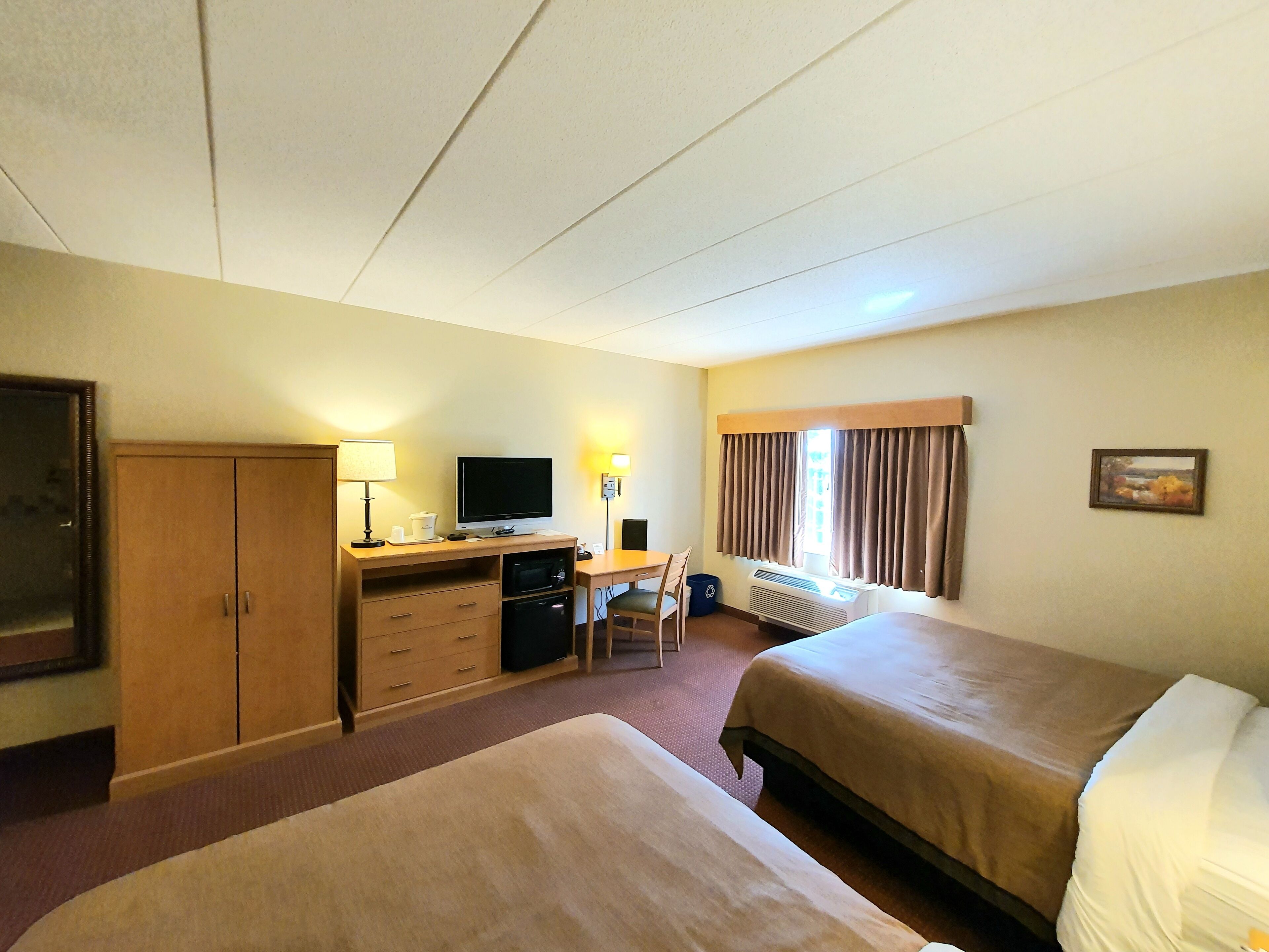 A hotel room with two beds, a desk with a computer, a chair, a wardrobe, and a window with curtains.