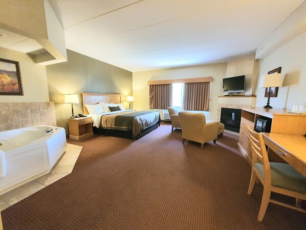 A hotel room with a large bed, a desk, a chair, a television, and a fireplace. - AmeriVu Inn & Suites - Waconia (Waconia)