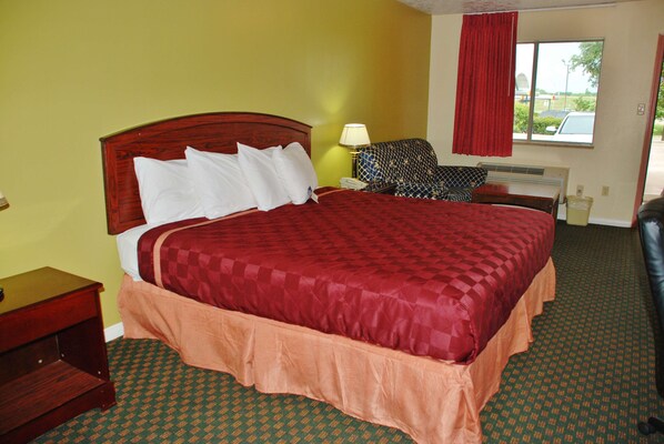 A hotel room with a large bed, a nightstand, a lamp, a chair, and a window with a view of the outside.
