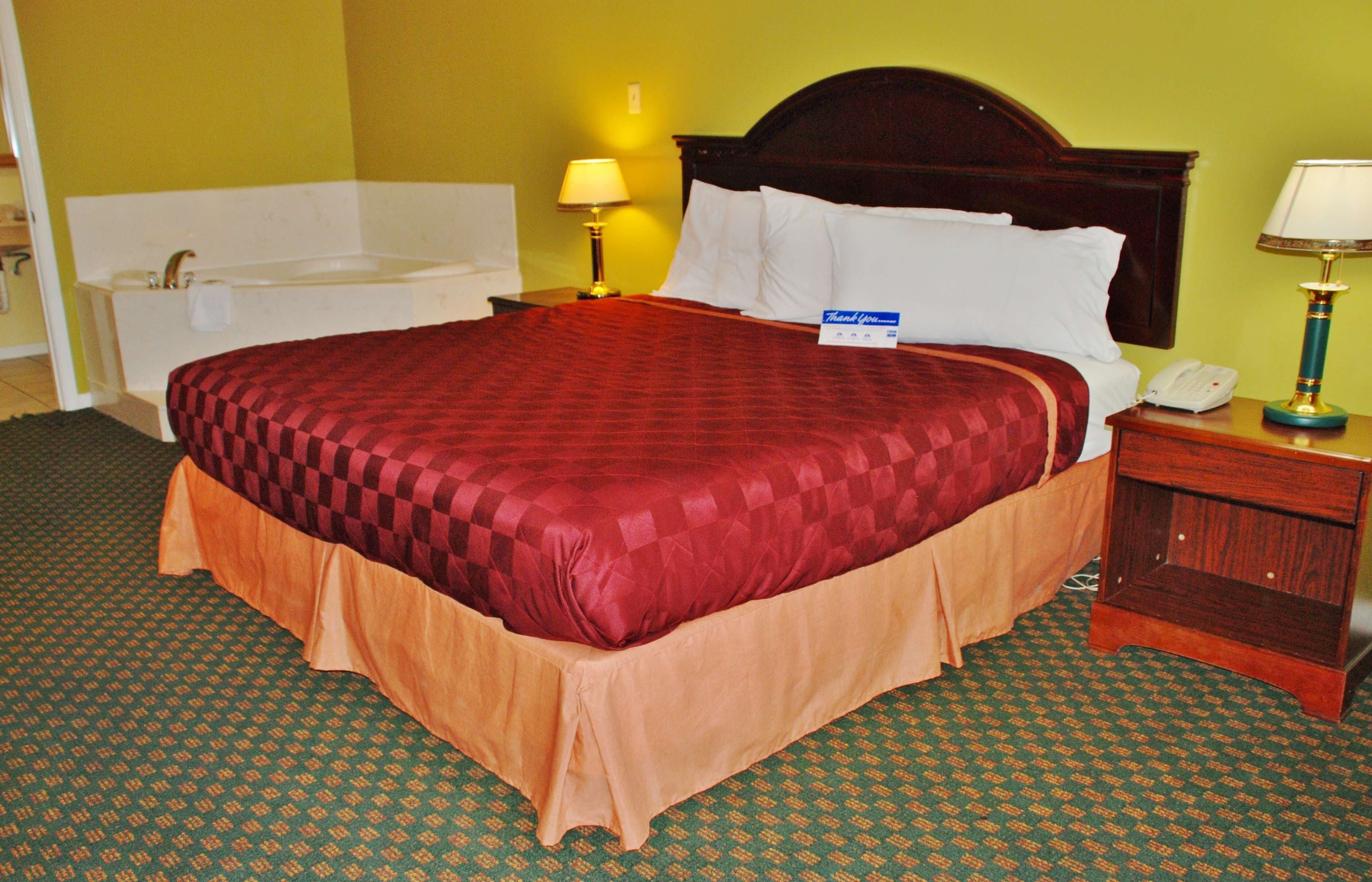 Ein Hotelzimmer mit einem großen Bett, einem Nachttisch mit Lampe, einem Telefon und einem Badezimmer mit Badewanne.