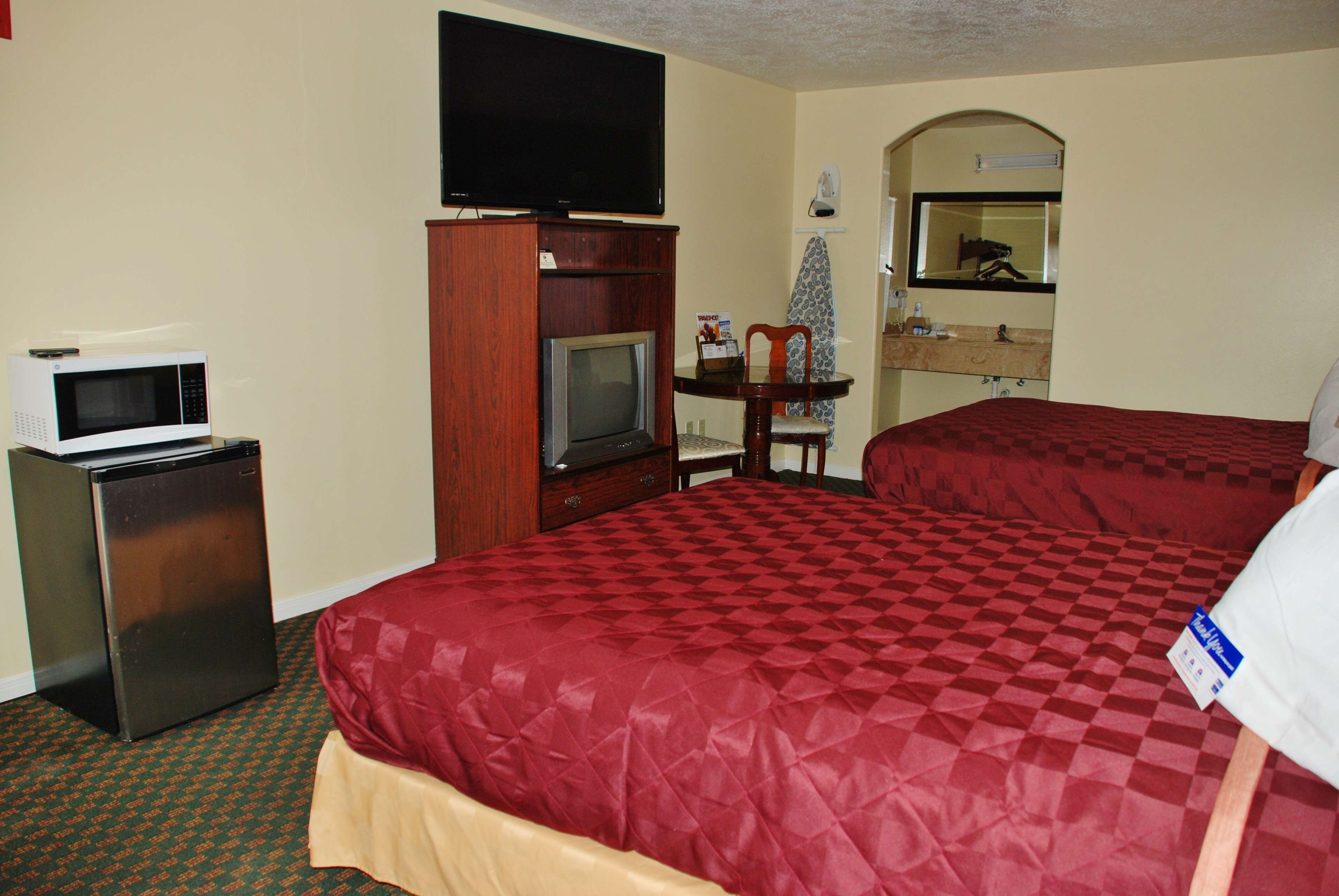 A hotel room with a bed, a television on a stand, a microwave, and a small refrigerator.