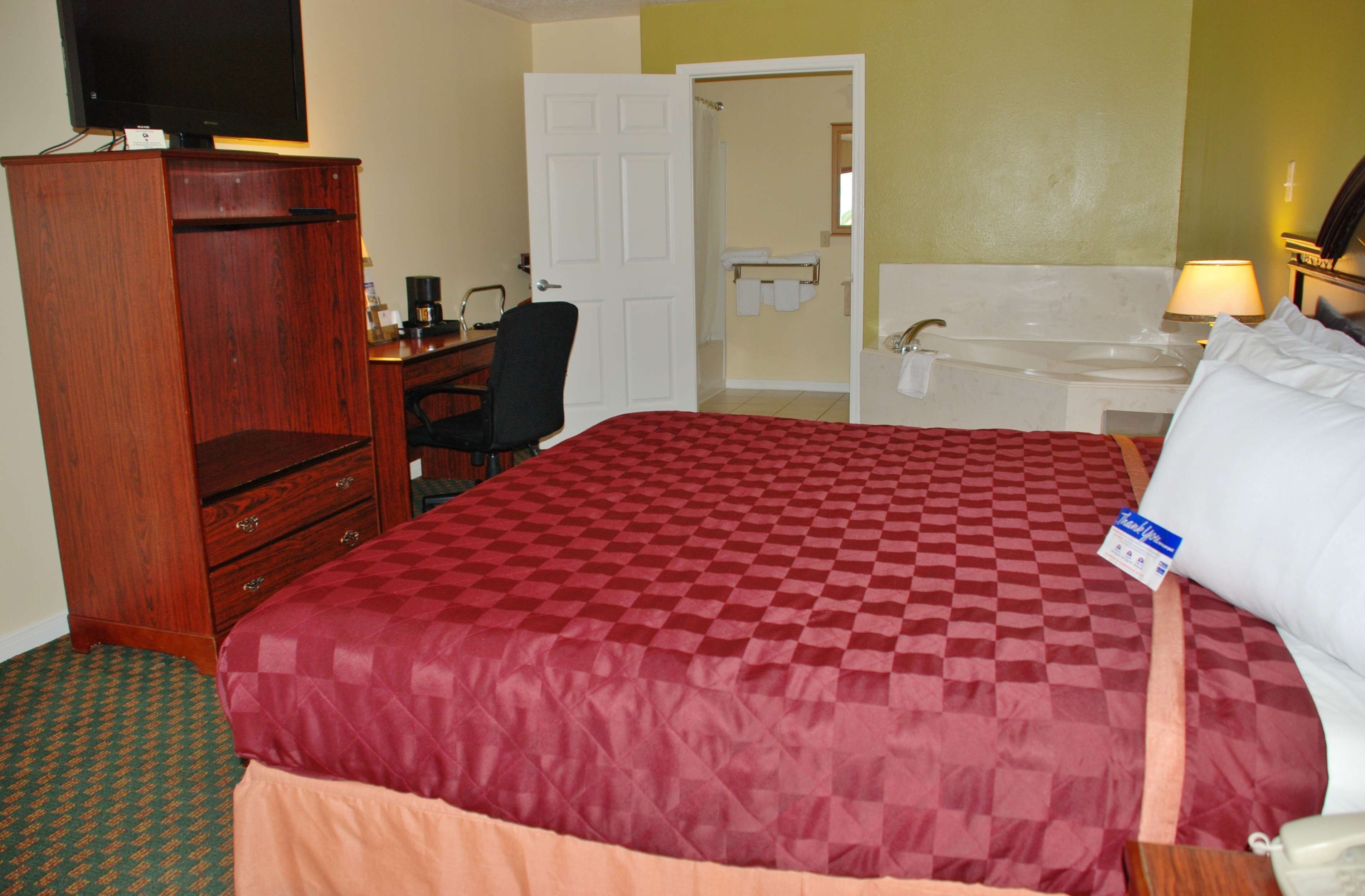 Habitación de hotel con una cama grande, un aparador de madera, un escritorio con una silla, un baño con bañera y un televisor sobre el aparador.