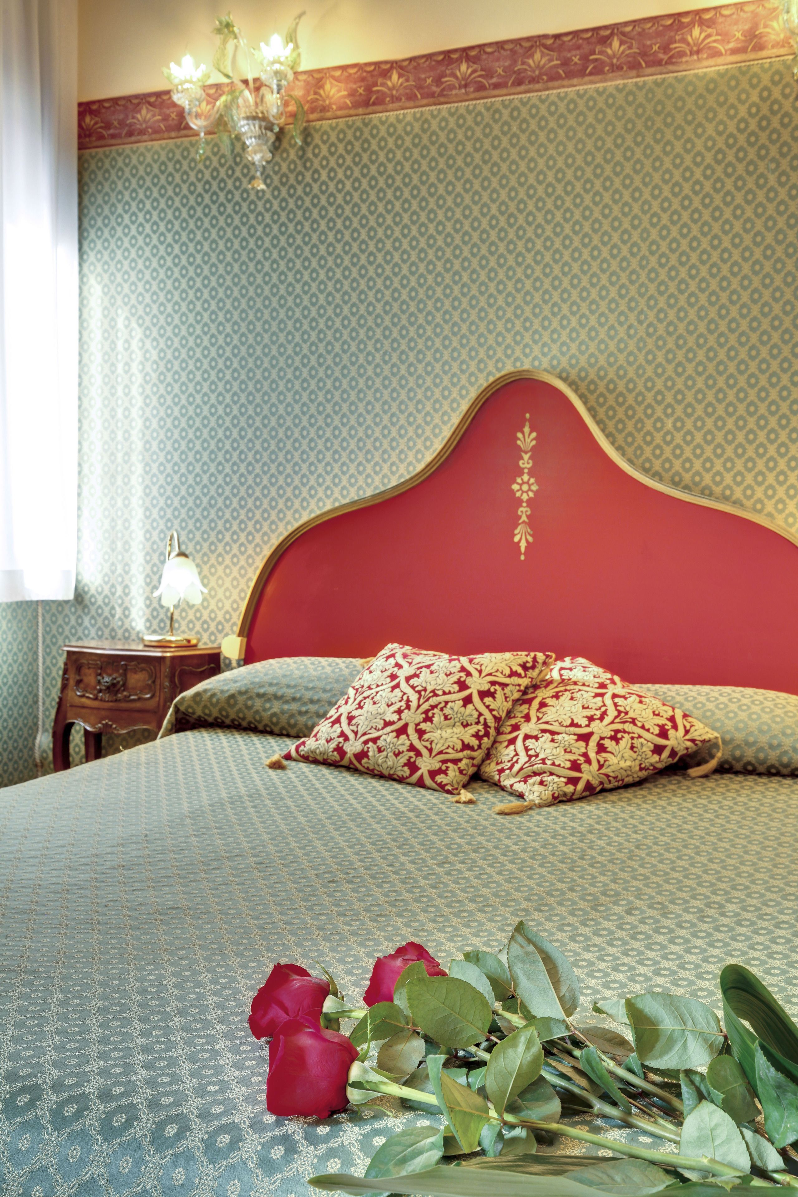 Quarto com papel de parede estampado, cabeceira vermelha e mesa de cabeceira com abajur.