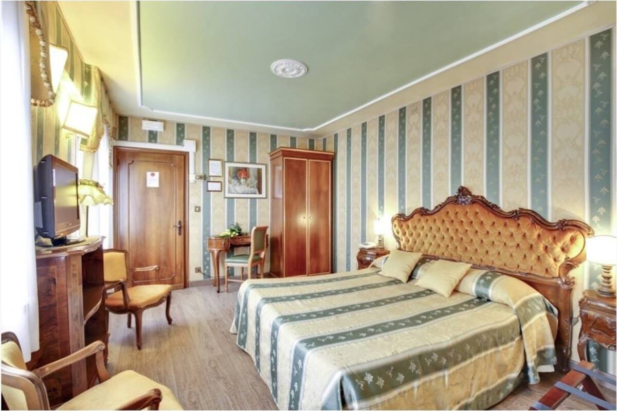 Habitación de hotel con una cama grande, un escritorio con silla, un armario y un televisor.