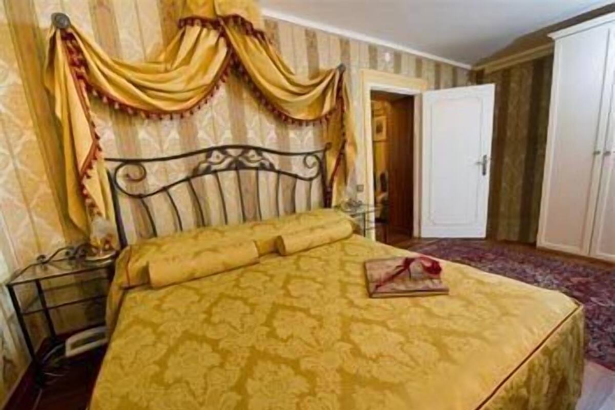 Una cama con una colcha estampada, una mesita de noche con una lámpara y un armario en una habitación con papel tapiz a rayas.