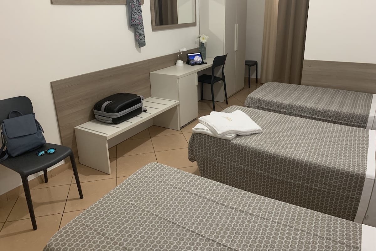 A hotel room with two beds, a desk, a chair, a small table, and a wardrobe.