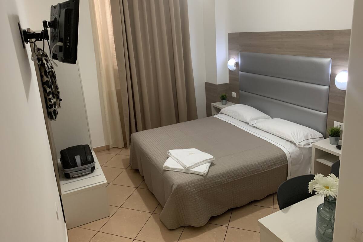 A hotel room with a bed, a desk, a chair, a TV, and a curtain.