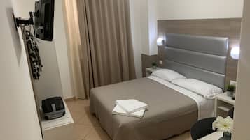 A hotel room with a bed, a desk, a chair, a TV, and a curtain.
