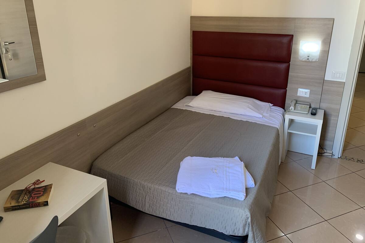 A neatly made bed with a headboard, a bedside table with a lamp, and a book on a small table.