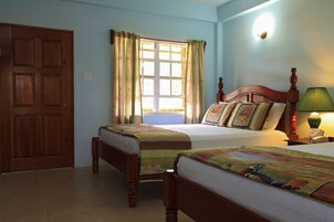 Un dormitorio con dos camas individuales, una puerta de madera, un ventanal con cortinas, una lámpara de noche y un aplique de pared.
