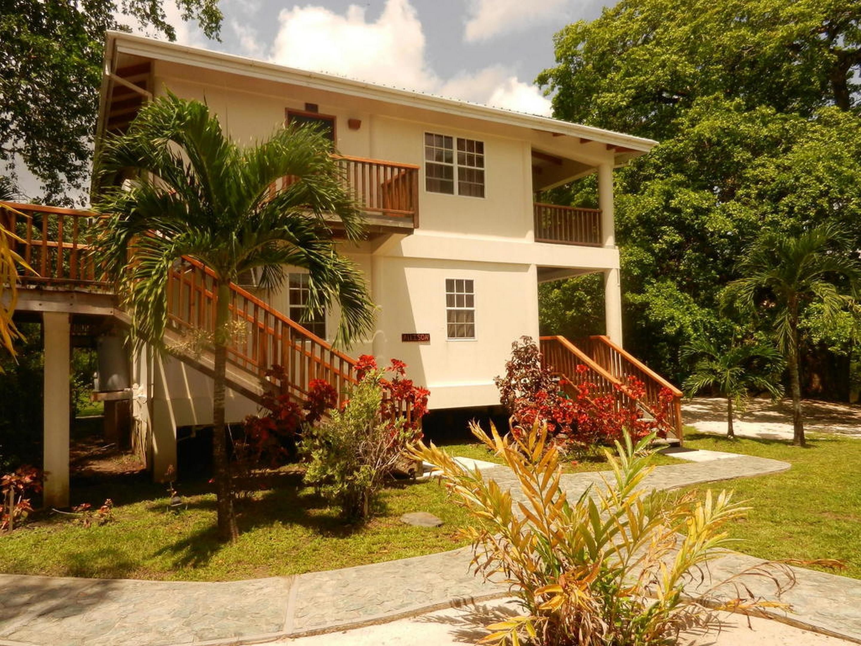 A two-story house with a balcony, surrounded by greenery and a well-maintained lawn.