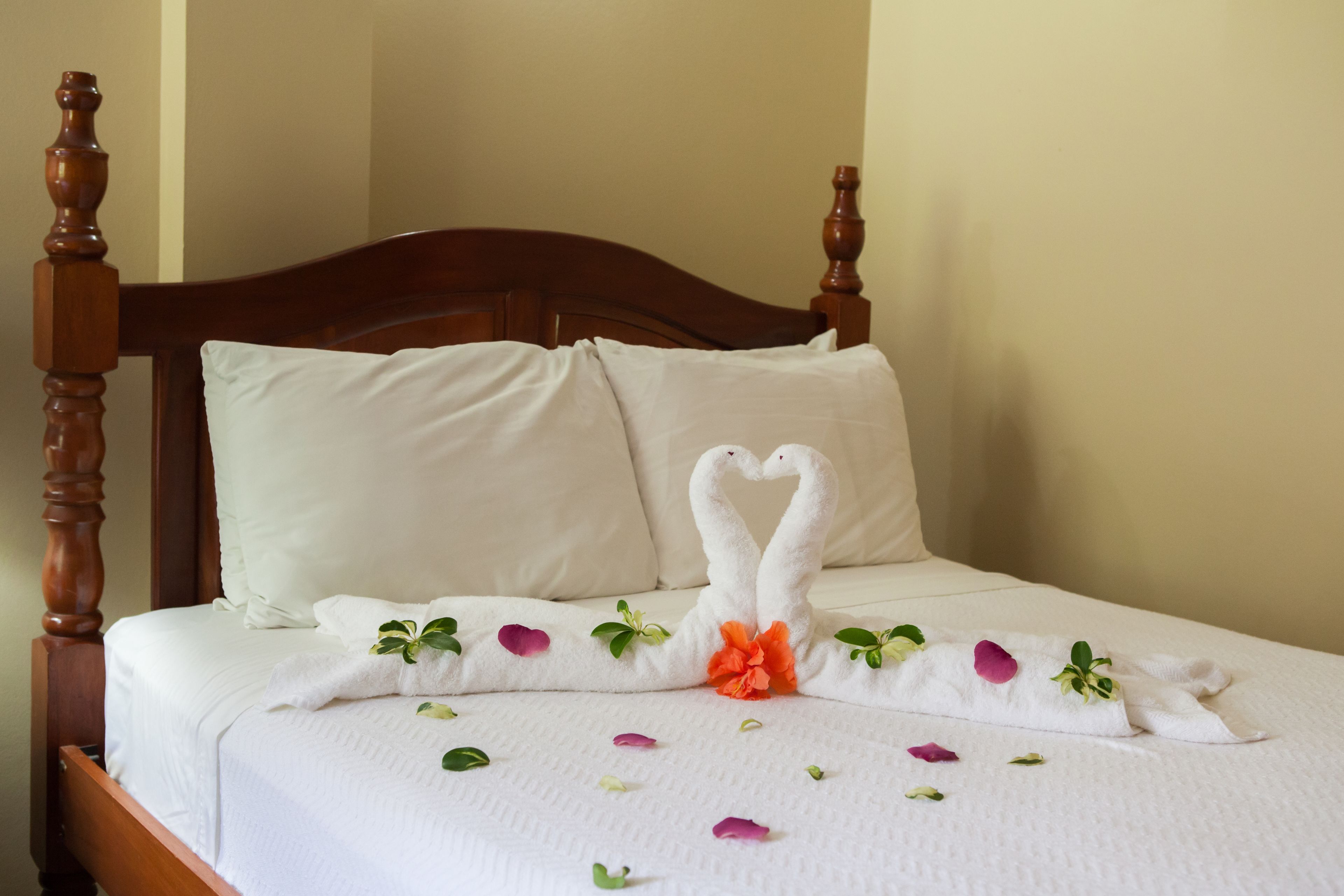 A neatly made bed with a white bedspread, two pillows, and a decorative towel arrangement featuring swans and flowers.