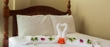 A neatly made bed with a white bedspread, two pillows, and a decorative towel arrangement featuring swans and flowers.