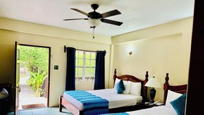 A hotel room with two beds, a ceiling fan, a window with curtains, a bedside lamp, and a view of greenery outside. - Black Orchid Resort (Burrell Boom)