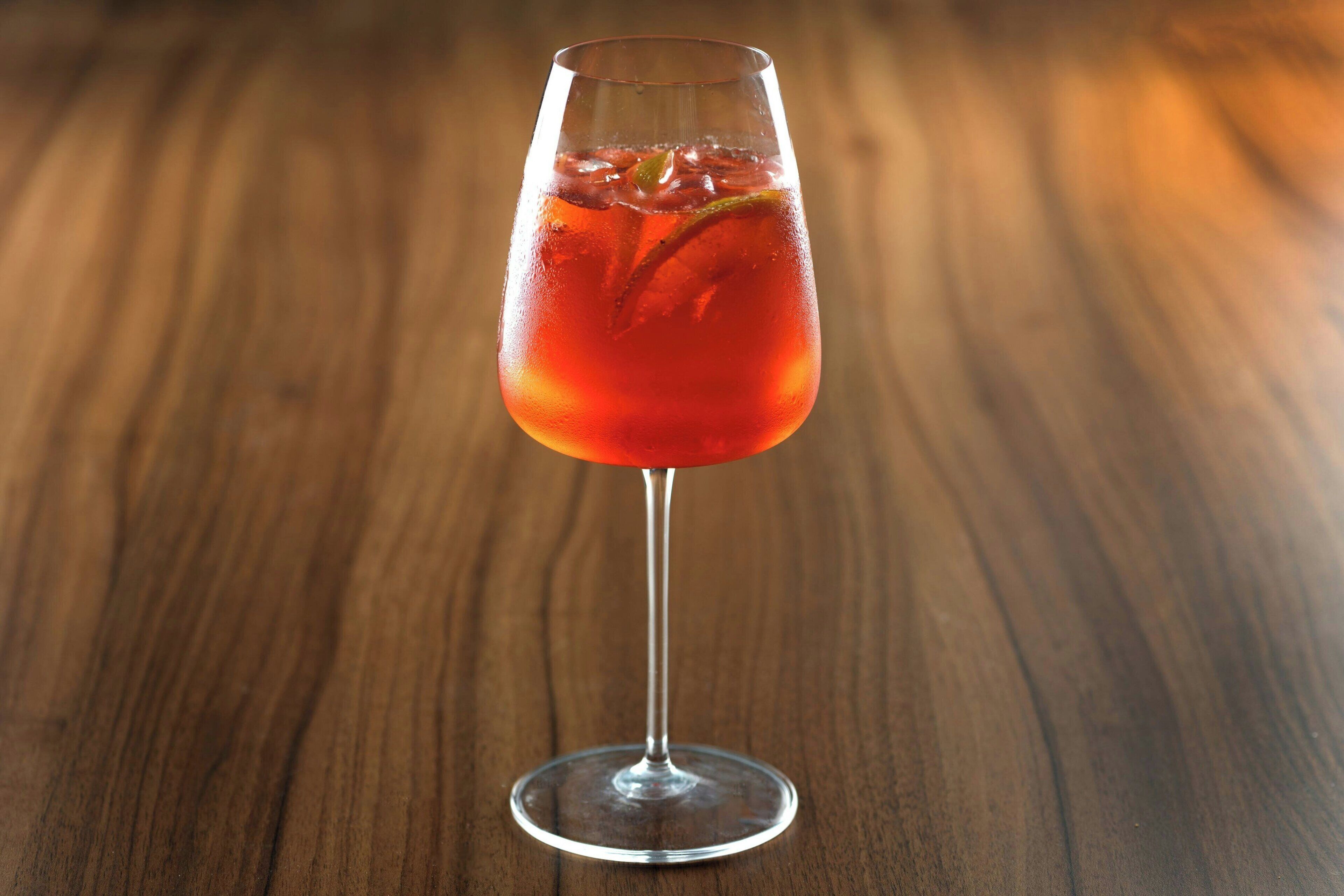 A clear glass of red beverage on a wooden surface.