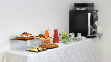 Monipuolinen aamiaisbuffet, jossa on tarjolla erilaisia ruokia, kahvinkeitin ja juomavesiautomaatti.