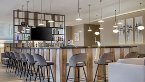 A bar area with a long counter, multiple bar stools, and a television screen. - AC Hotel by Marriott Milan Sesto (Sesto San Giovanni)