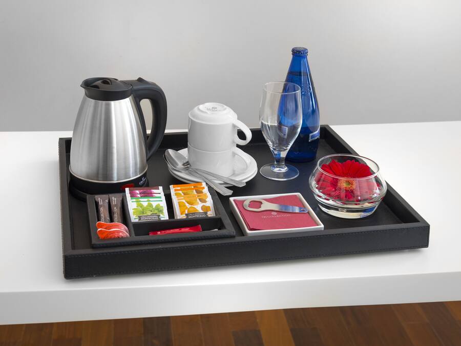 Una bandeja con una cafetera, tazas, un vaso, una botella y otra bandeja con alimentos y una tarjeta.