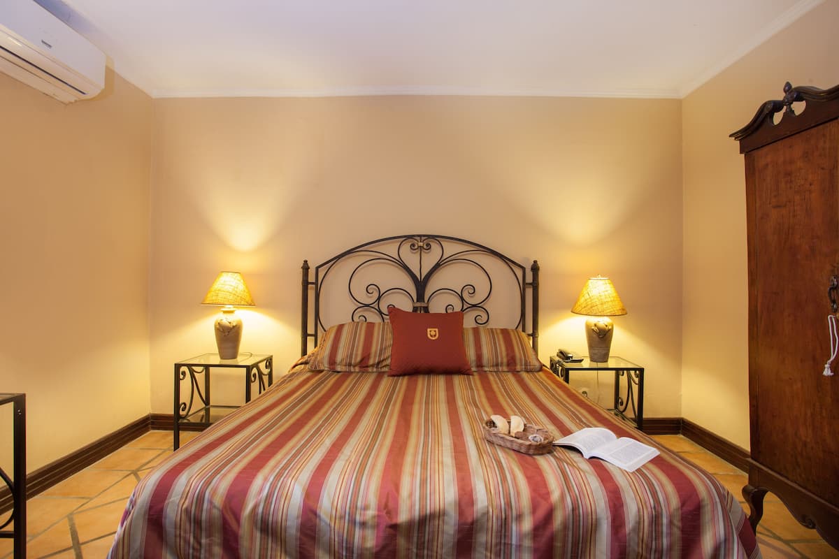 A neatly made bed with striped bedding, two bedside lamps, and a wooden wardrobe.