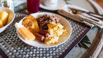 A breakfast plate with eggs, sausage, and toast on a woven table mat.