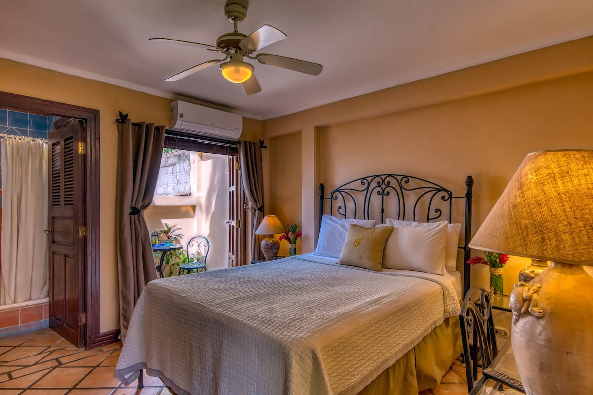 A neatly arranged bedroom with a bed, ceiling fan, bedside lamps, and a window with curtains.