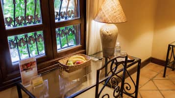 Uma mesa com tampo de vidro, uma cesta de frutas, uma luminária e uma garrafa.