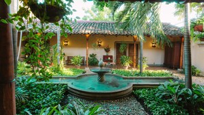 A courtyard with a fountain, surrounded by lush greenery and a building with a tiled roof. - Los Robles Charming Colonial Boutique Hotel (Managua)