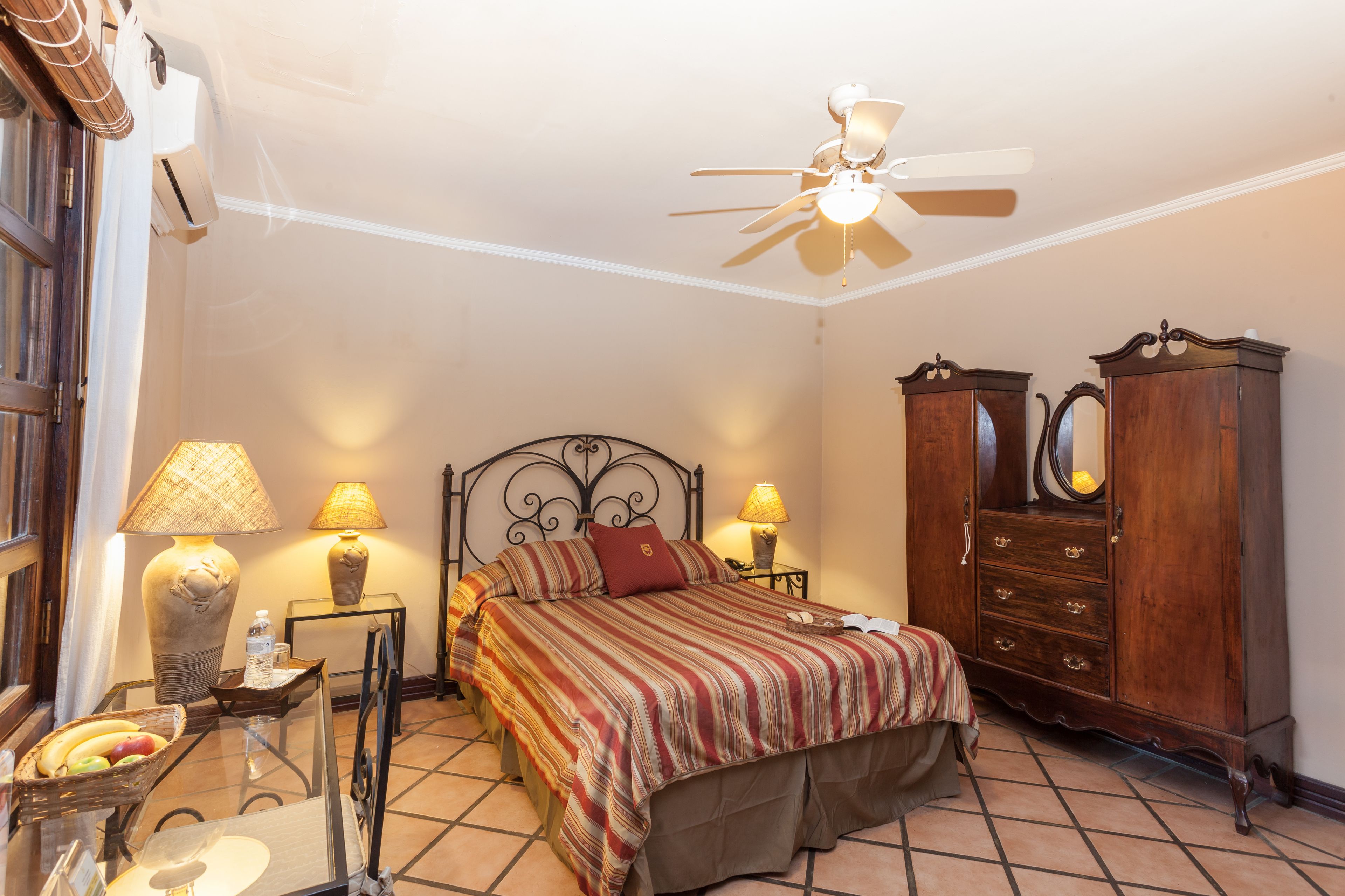 Un dormitorio con cama, lámparas de noche, armario de madera y ventilador de techo.