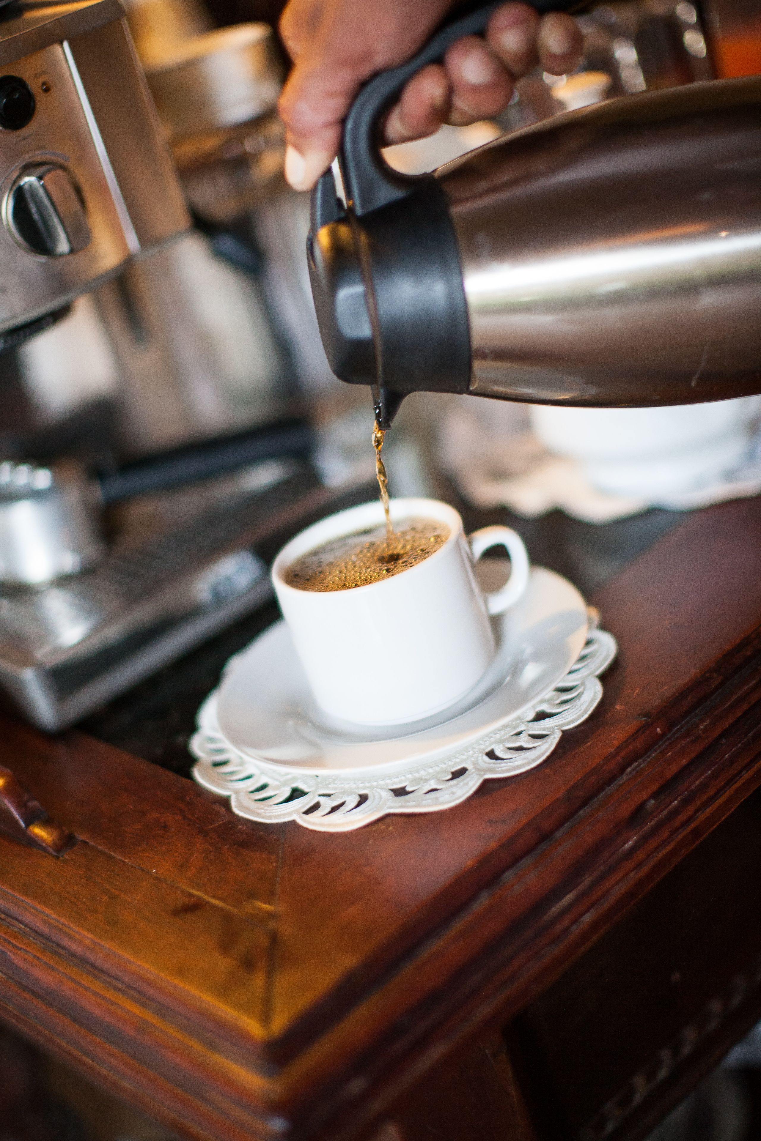 Mão servindo café em uma xícara sobre mesa de madeira.