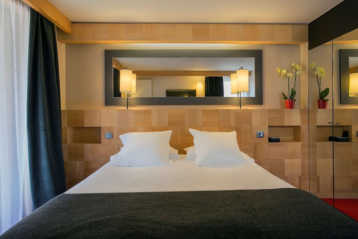 A hotel room with a large bed, two bedside lamps, a mirror, and a small potted orchid.